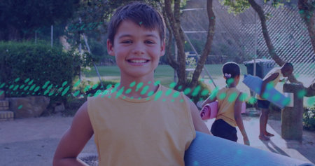 Smiling boy carrying blue yoga mat at outdoor playground, with water fountain and stone bench. Playground, friendship, outdoor, children, exercise, vitality, leisureの写真素材