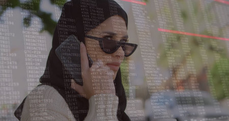 Talking woman wearing headscarf and sunglasses using smartphone in cafe, with digital code overlay. Technology, communication, connectivity, urban, modern, lifestyle, professionalの写真素材