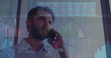 Holding smartphone to ear man in shirt scanning data graphics on metal-frame glass panels in office....