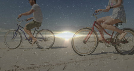 Pedaling couple in summer clothes riding across sandy beach, with red and blue cruiser bicycles. Romance, leisure, outdoor, scenic, relaxation, adventure, leisurewearの写真素材