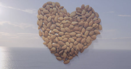 Heart-shaped cluster of whole almonds resting on shore at coastal vista, with calm ocean reflection. Organic, natural, health, wellness, minimalist, serenity, outdoorの写真素材