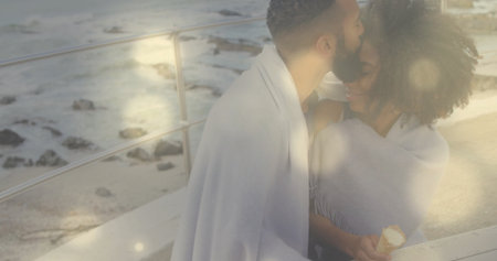 Kissing couple holding ice cream in blanket against metal railing on coastal walkway, copy space. Romantic, affection, leisure, seaside, sunset, warmth, serenityの写真素材