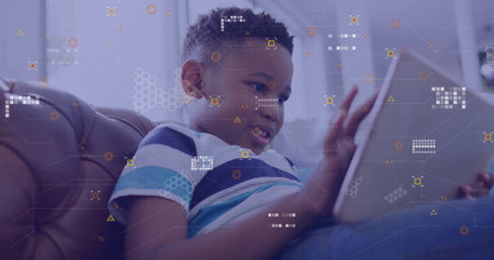 Holding tablet boy wearing blue striped shirt and jeans leaning on brown leather sofa at home. Children, technology, modern, casual, domestic, relaxation, educationalの写真素材