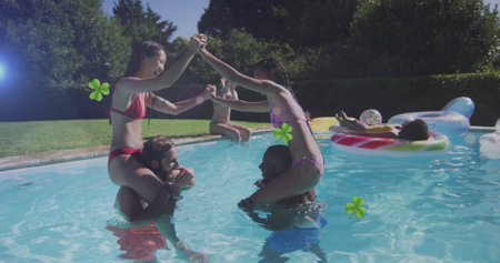 Two couples wearing swimwear playing shoulder balancing game in backyard pool, inflatable ring....