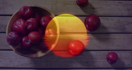 Displaying wooden bowl holding red plums on worn plank table showing glitch sun overlay, copy space. Rustic, natural, vibrant, organic, artistic, harvest, freshnessの写真素材