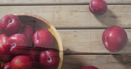 Displaying wooden bowl holding red plums on rustic tabletop, with scattered plums, copy space. Fruit, harvest, organic, healthy, rustic, natural, snackの写真素材