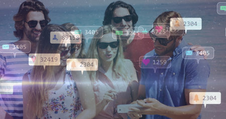 Leaning in six friends wearing sunglasses viewing smartphone on beach, with social media icons. Sunset, celebration, connection, summer, leisure, technology, lifestyleの写真素材