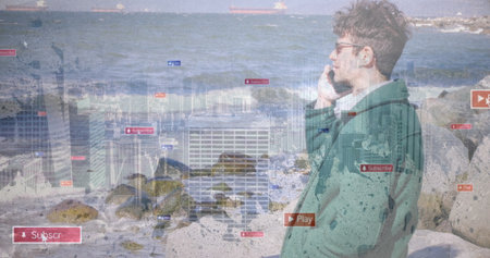 Green jacketed man in eyeglasses holding smartphone and viewing UI icons on rocky shore, copy space. Adventure, technology, communication, maritime, digital, lifestyle, navigationの写真素材