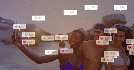 Smiling four friends posing for group selfie on sandy beach at sunset with smartphone notifications....