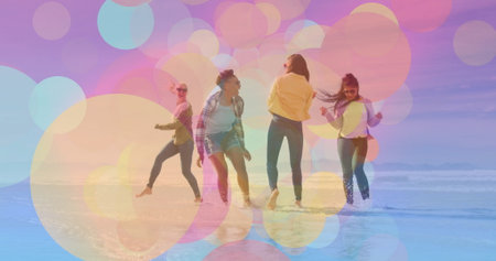 Dancing four friends splashing in shallow water at beach shoreline, with windbreaker and shorts. Joy, celebration, leisure, vibrancy, outdoor, lifestyle, motionの写真素材