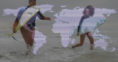 Wading women carrying surfboards through shallow water at shoreline, with wetsuits and surf leashes. Beach, coastal, ocean, waves, adventure, friendship, lifestyleの写真素材