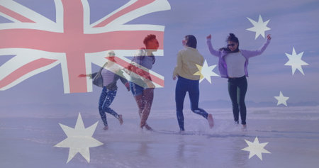Frolicking women wearing casual jackets splashing in shallow surf at beach, with Australian flag. Beach, friendship, carefree, summer, outdoor, happiness, lifestyleの写真素材