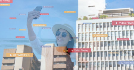 Woman wearing sun hat taking smartphone selfie by ocean with Get Notified and Friend Added overlays. Beach, outdoor, leisure, modern, technology, lifestyle, tranquilityの写真素材