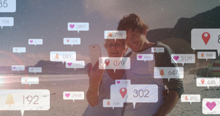 Posing mother-son duo taking selfie on beach at sunset, with smartphone floating notification icons. Family, communication, leisure, outdoor, nostalgia, tranquility, digitalの写真素材