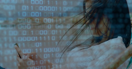 Asian woman wearing knit sweater holding smartphone under binary code overlay in car cabin headrest. Technology, connectivity, data, digital, modern, commute, communicationの写真素材