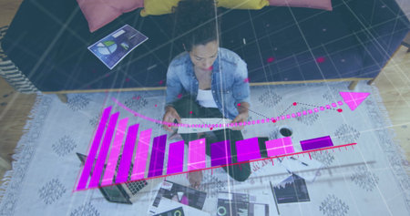 Analyzing woman wearing denim shirt, reviewing data at home, with tablet and 3D graphs. Modern,...