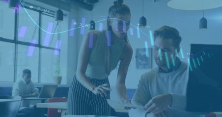 Teenage female wearing green top and colleague collaborating in open office, with printed charts. Collaboration, teamwork, analytics, data, workspace, modern, professionalの写真素材