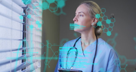 Reviewing data doctor in scrubs holding tablet at clinic window, with hologram overlays, copy space. Healthcare, technology, innovation, professionalism, diagnostics, digital, medicalの写真素材