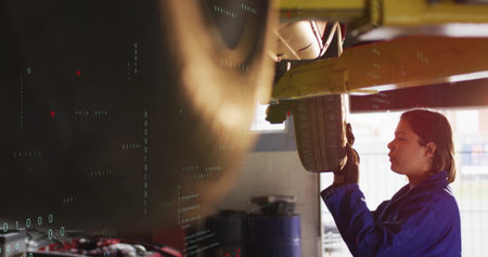 Mechanic in coveralls inspecting tire on lift at shop with oil barrels, work gloves, copy space. Industrial, maintenance, tools, safety, professional, diagnostic, technicalの写真素材