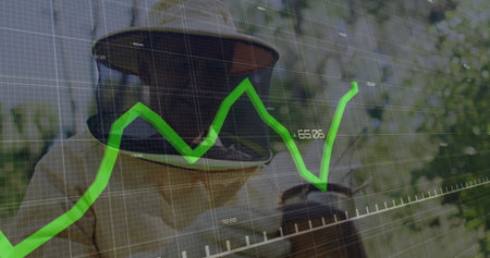 Holding metal smoker, beekeeper wearing protective suit in garden apiary, with green graph overlay. Apiary, agriculture, safety, data, outdoor, environmental, technologyの写真素材