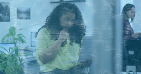 Reviewing woman wearing light green blouse marking paper documents at desk, with pen and laptop....