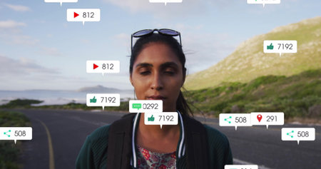 Standing travel vlogger wearing bomber jacket and backpack on coastal highway, with social icons....