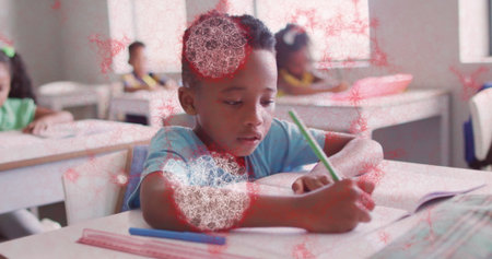 Writing boy in light blue shirt leaning over desk in classroom, with green pencil and notebook. Students, education, learning, literacy, academic, school, teamworkの写真素材