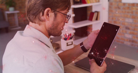 Holding tablet man wearing shirt and glasses at home office desk, with closed laptop and organizer....