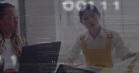 Colleagues reviewing printed documents and laptop in meeting room wearing mustard yellow overalls....