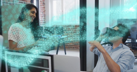 Coworkers collaborating with clipboard, wearing VR headset in office with monitors showing hologram. Innovation, collaboration, technology, workspace, creativity, teamwork, digitalの写真素材