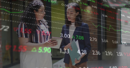 Comparing stock charts on tablet and folder by businesswomen in office, displaying market numbers....