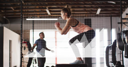 Jumping woman in tank top performing box jump onto plyometric box in gym with jump rope. Fitness, strength, cardio, training, motivation, industrial, modernの写真素材