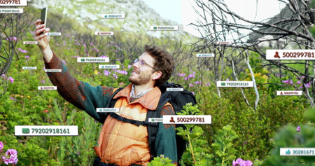 Holding smartphone, hiker in orange vest taking selfie on rocky slope with backpack, digital labels....