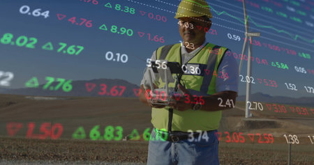 Operator in yellow helmet, neon vest operating tablet at wind turbine, overlaid data, copy space....
