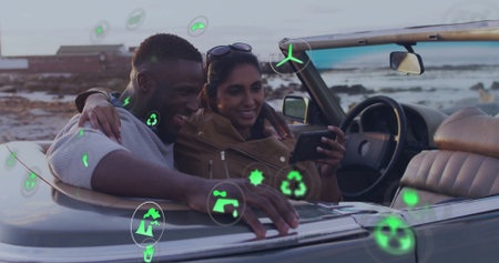 Leaning couple with sunglasses viewing smartphone in convertible by coast with floating green icons....