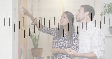 Coworkers in business attire pointing and gesturing in office meeting room, with sticky note board....
