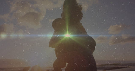 Parent silhouette lifting child upright on beach shoreline, with lens flare and scattered clouds. Family, connection, serenity, warmth, adventure, harmony, naturalの写真素材