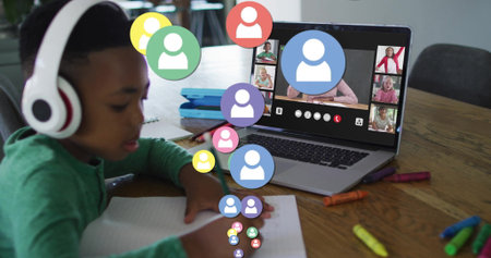 Writing boy wearing green shirt and headphones noting in notebook at home, with laptop, copy space. Education, distancelearning, remoteactivity, e-learning, digitalclassroom, youthful, innovativeの写真素材