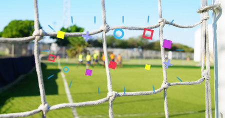 Framing soccer goal net with group of six players practicing on grass pitch, with neon bibs....