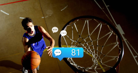 Leaping man in sportswear shooting basketball toward hoop at gym with speech bubbles 81, copy space. Athlete, action, competition, athleticism, gymnasium, sports, dynamicの写真素材