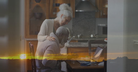 Collaborating couple working on laptop in kitchen area, with phone, papers, pen and glass of water. Partnership, collaboration, domestic, cozy, familial, work-life balance, modernの写真素材