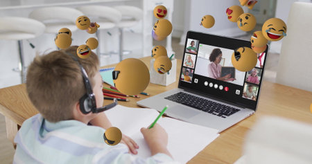 Writing boy in headset leaning over paper at home table, with laptop and pencils, floating emoji....