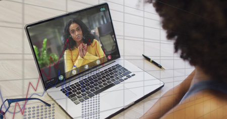 Displaying laptop showing woman in yellow blazer speaking at home office call with pen and graphs. Collaboration, communication, digital, analytics, professionalism, technology, workspaceの写真素材