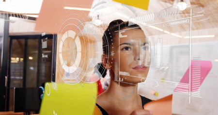 Woman in black sleeveless top arranging sticky notes on glass partition in office, with UI overlay....
