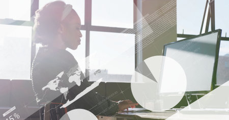 Typing woman wearing top at office window, with monitor showing overlaid data graphics, copy space. Professional, data analysis, modern, technology, workspace, urban, digitalの写真素材