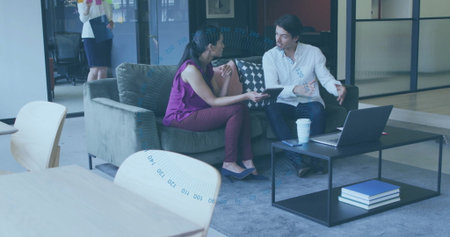 Colleagues in businesswear reviewing project plan on tablet in office lounge, with coffee cup....