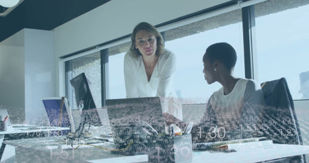 Collaborating professional women analyzing documents on laptops at office desk, with data overlay. Business, teamwork, modern, technology, communication, productivity, corporateの写真素材