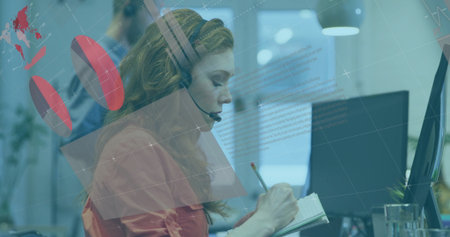 Writing woman wearing orange blouse and headset taking notes in spiral notebook at desk, copy space....