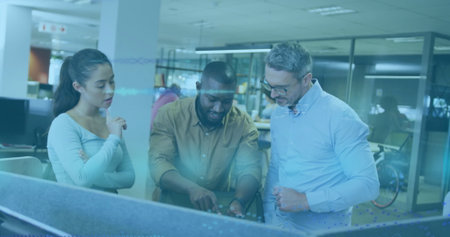 Pointing at digital display, three colleagues collaborating at modern office desks, with bicycle....