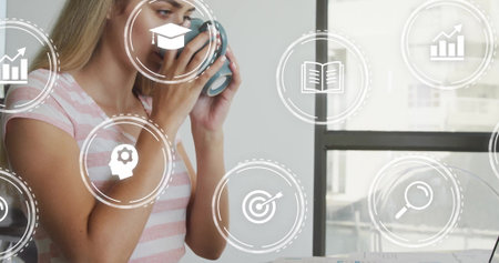 Sipping woman wearing striped t-shirt at office desk, holding mug with analytics icons, copy space....